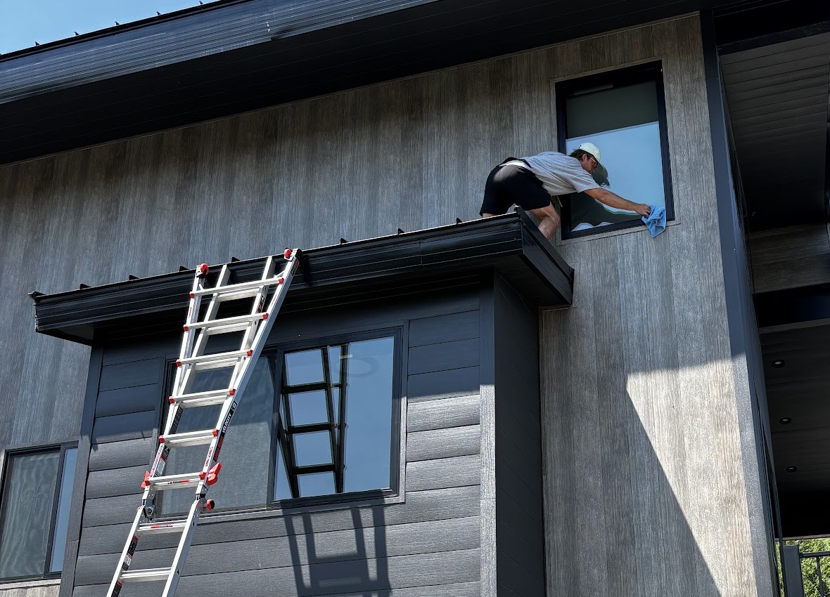 RAVI technician on a ladder cleaning a high window on a modern home